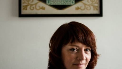 Image of Eimear McBride sitting below a framed cross-stitch reading 'The Way to Theatreland by Underground'