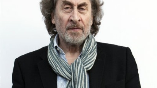 Image of Howard Jacobson with a large grey- and white-striped scarf, frowning slightly at the camera