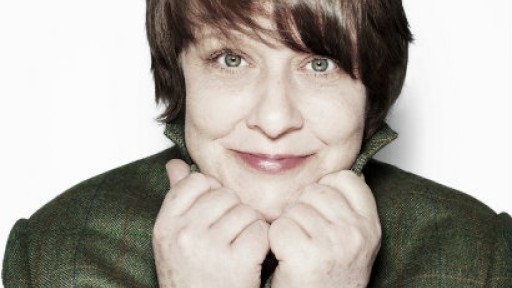 Headshot of Kathy Burke, holding her collar with her hands under her chin